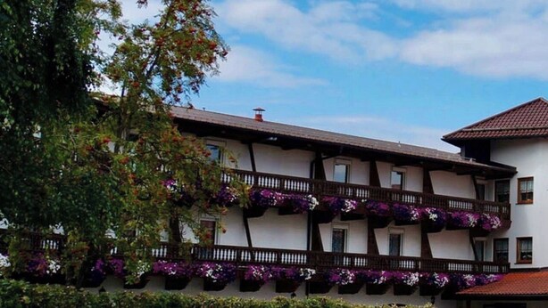 A traditional building with multiple balconies adorned with flowers, a paved courtyard, and a clear sky. - Furnished apartment for 1 person (Büchlberg)