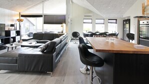Eine moderne Küche mit Holzarbeitsplatte und Barhocker, einem großen Esstisch sowie einem eingebauten Backofen.