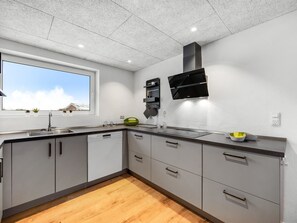 A modern kitchen with grey cabinets, a dishwasher, a window with a view of a building, and a black range hood.