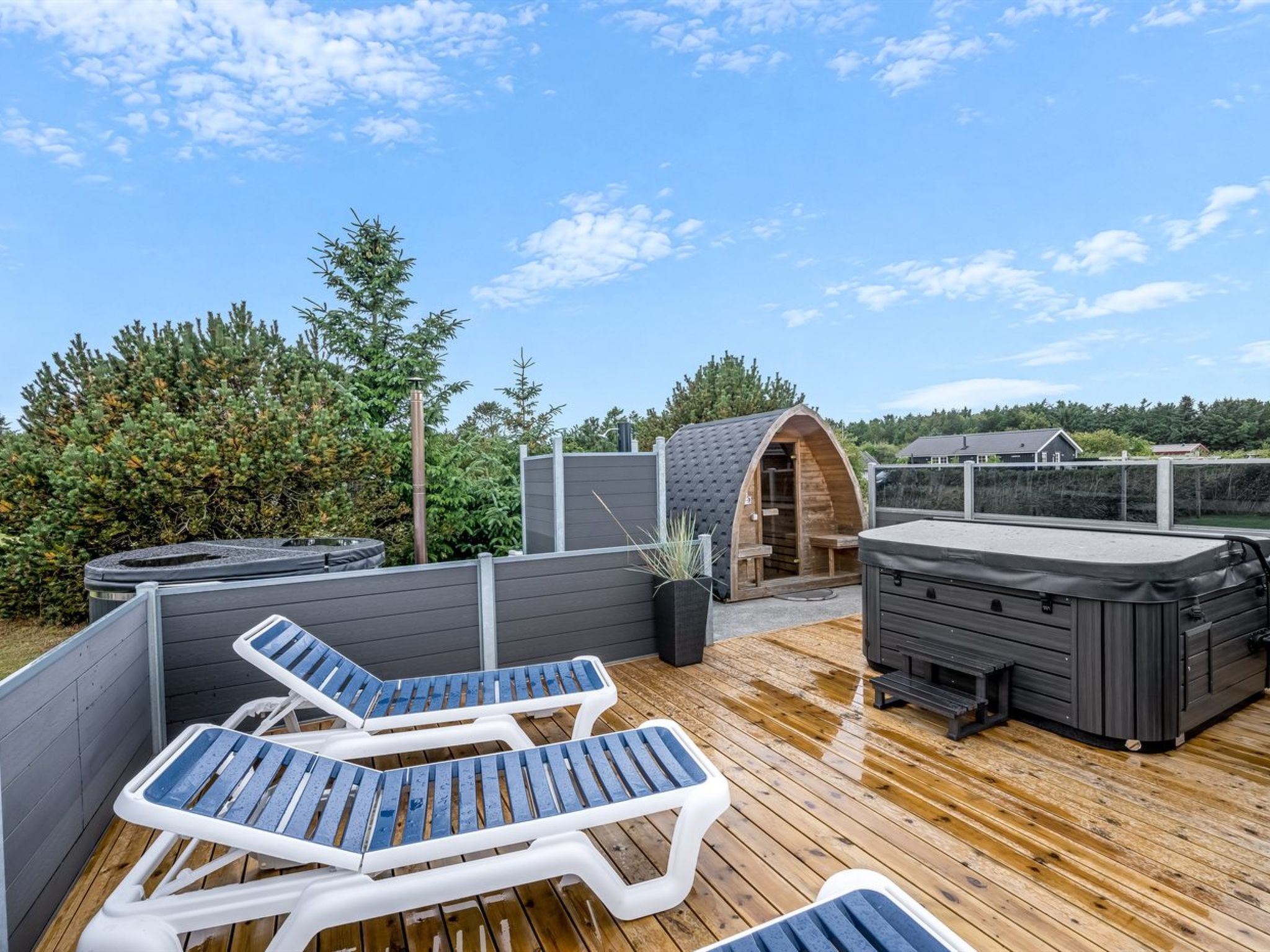 A wooden deck with lounge chairs, a hot tub, and a sauna.