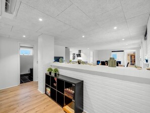A spacious room with a high ceiling, a wooden floor, and a white brick wall. There is a black entertainment unit with a chessboard and a small plant.