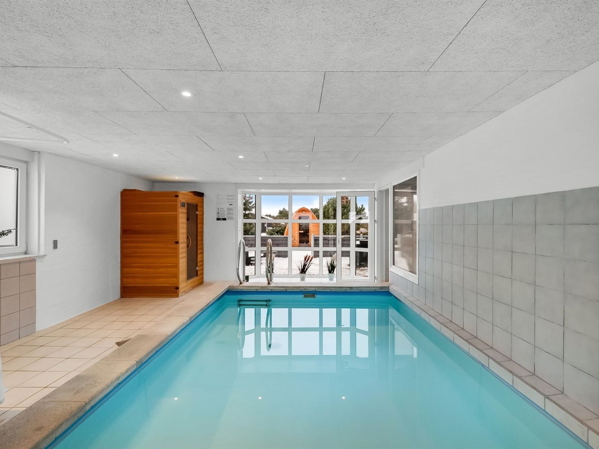 Ein Schwimmbad mit einer Holzzu sauna, Blick auf ein Haus und eine geflieste Wand.