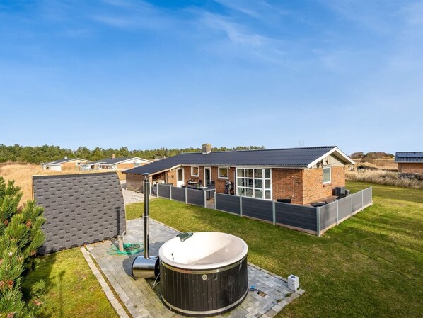 A residential property with a large hot tub, a covered patio, and a brick house with a sloped roof.