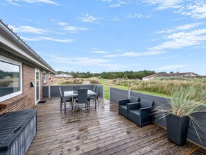 A covered outdoor patio with a wooden deck, a table with chairs, and a potted plant.