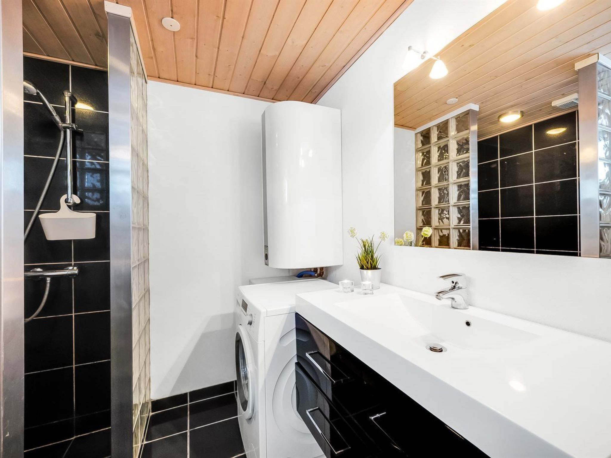 A modern bathroom with a built-in washer and dryer, a large mirror, and a shower with a handheld showerhead.