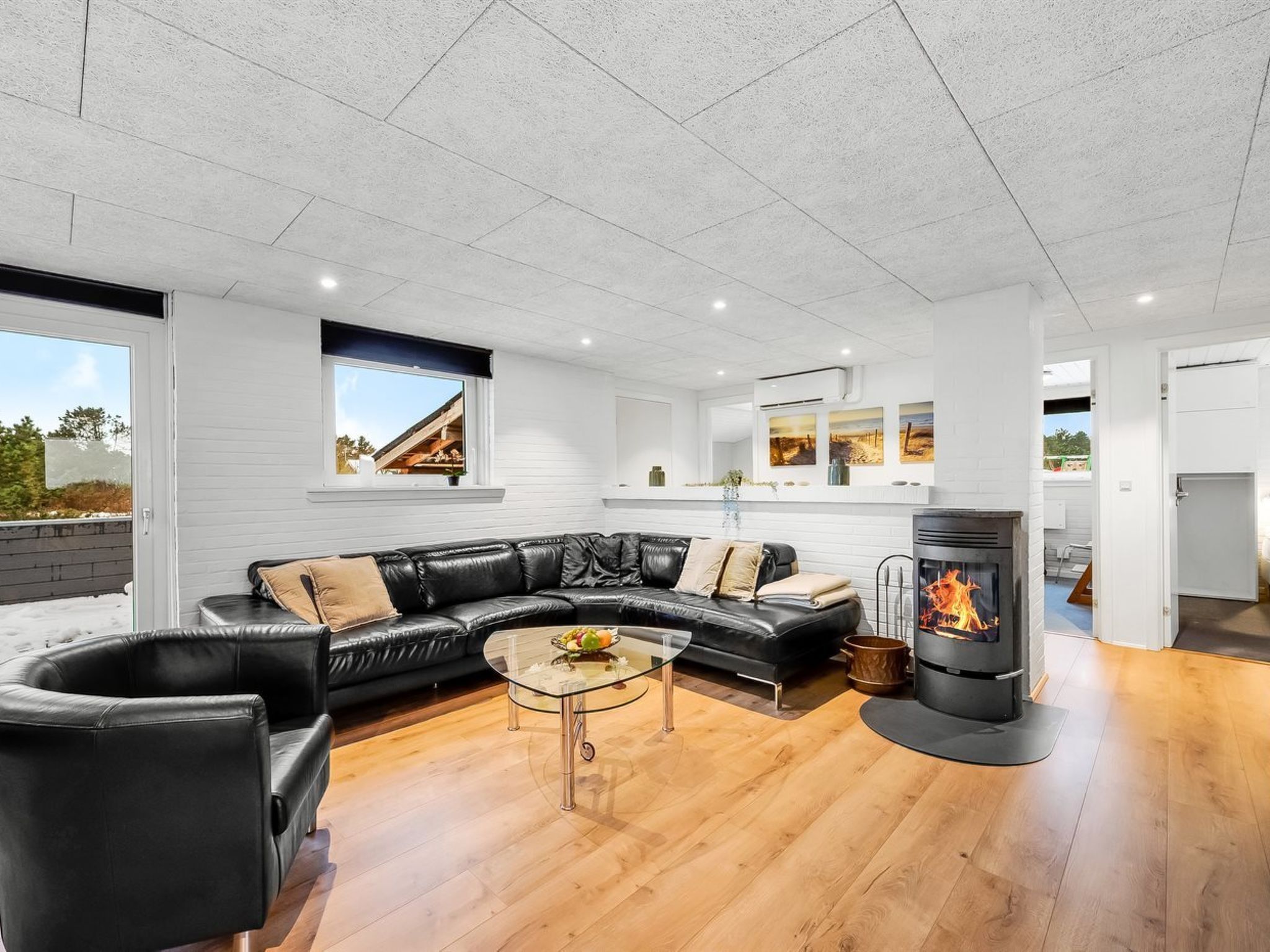 A modern living room with a black leather sofa, a glass coffee table, and a wood-burning stove.