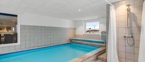 Piscina com área de chuveiro, paredes revestidas e janela com vista.