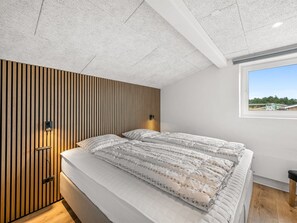 A bedroom with a bed, wooden slat wall, ceiling light, and a window with a view.