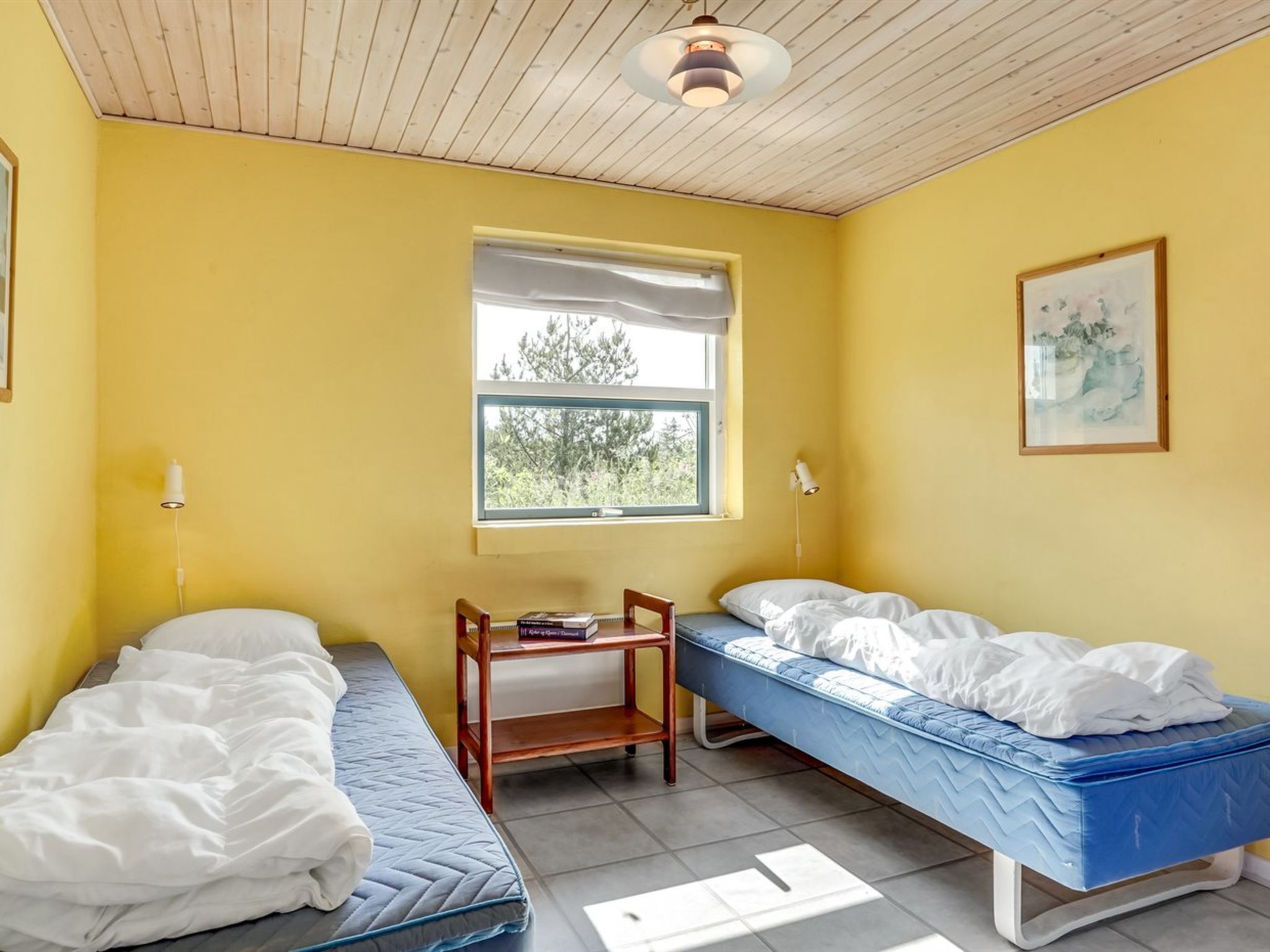 A room with two beds, a window, a small table, and a ceiling light.