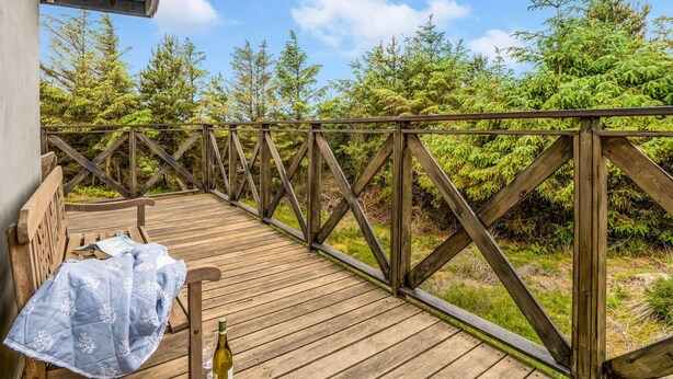 Eine Holzterrasse mit Geländer, einer Bank und einer Weinflasche.