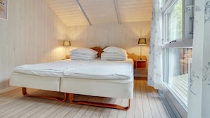 A double bed with two nightstands, each with a lamp, in a room with wooden walls and floors. - "Selver" - 250m from the sea by Interhome (Hals)