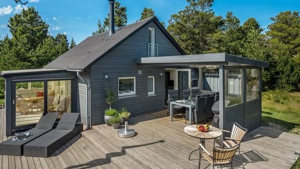 A modern house with a deck, outdoor seating, and a small covered area with a grill.