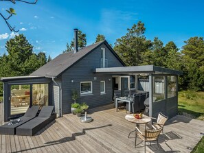 Una casa moderna con terraza, mobiliario exterior y un área cubierta pequeña con una parrilla.