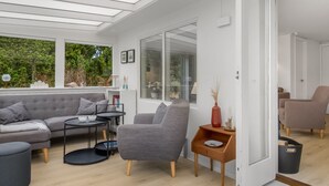 A modern living room with a sofa, armchair, side table, and a glass door leading to another room.