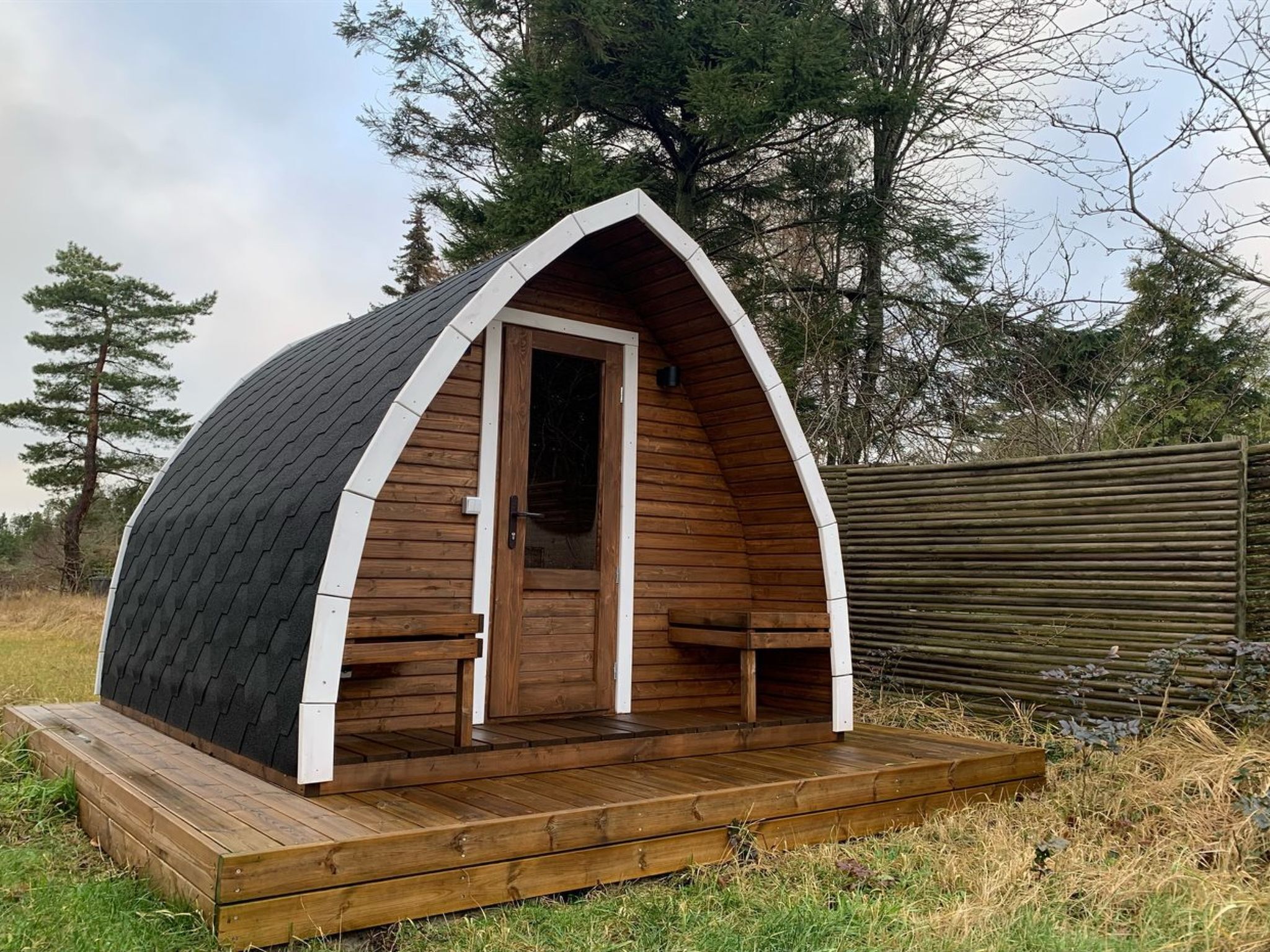Een klein houten vakantiehuisje met een schuine kap, een voordeur en een houten terras.
