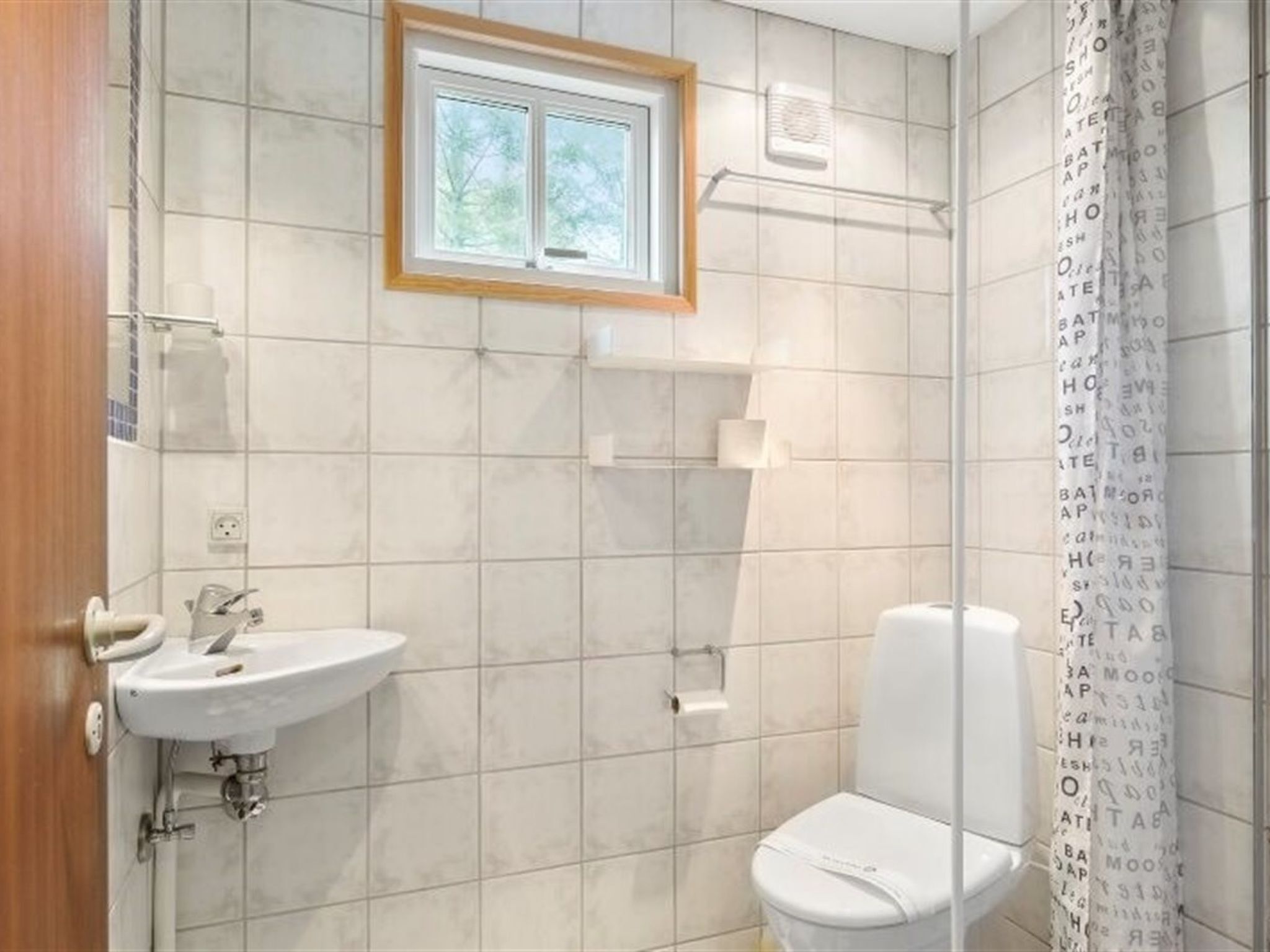 A bathroom with a white sink, toilet, and shower. There is a window above the sink and a towel rack on the wall.