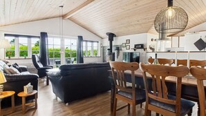 Amplia sala de estar con un sofá negro, sillas de comedor de madera y un ventanal con vistas a la vegetación.