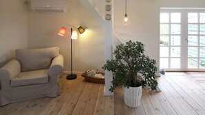 A living room with a beige sofa, a floor lamp, a potted plant, and a large window with a view. - "Harre" - 300m from the sea by Interhome (Rudkøbing)