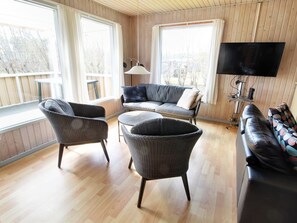 Ett mysigt vardagsrum med en soffa, två fåtöljer, ett soffbord och en tv.