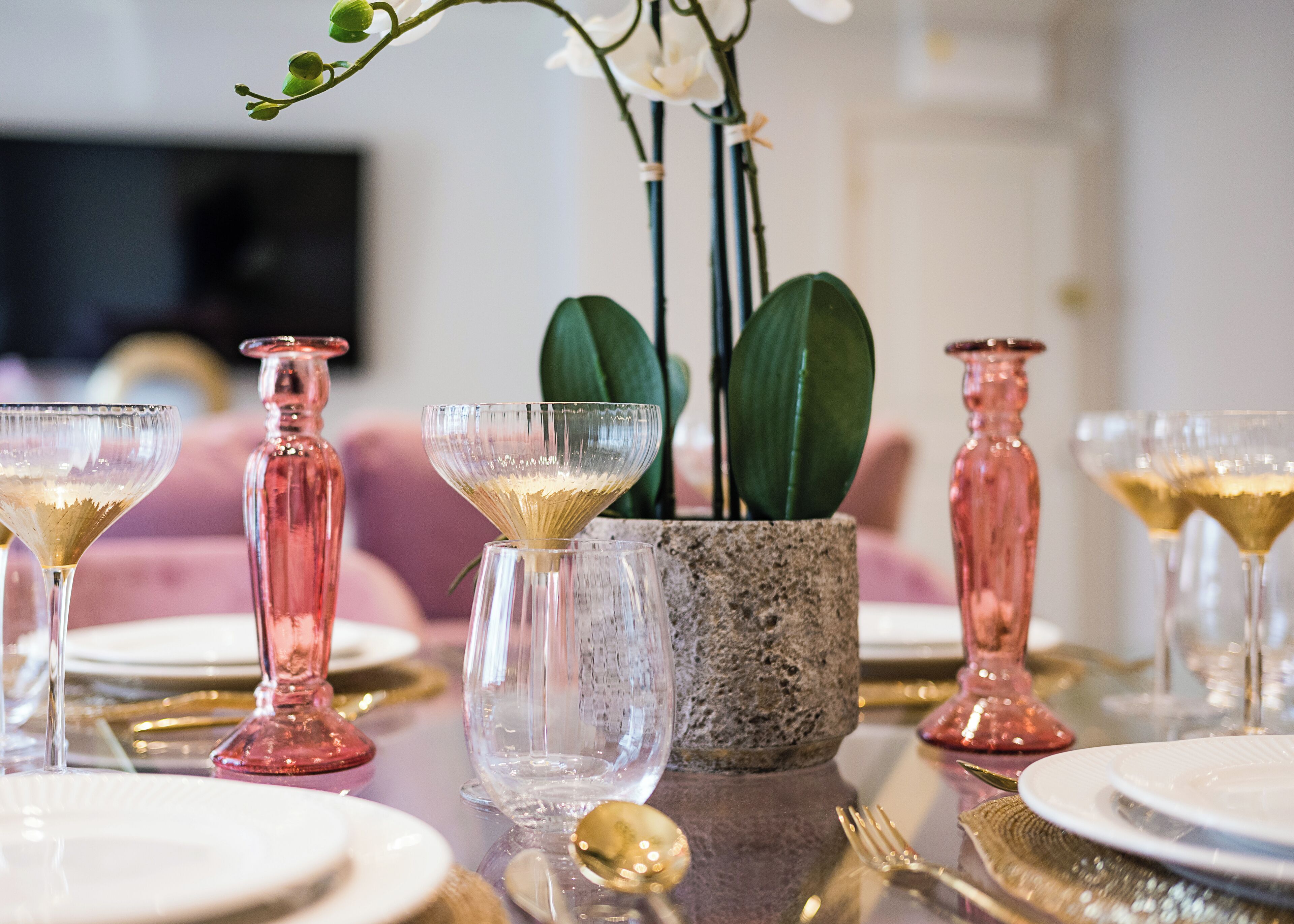 A dining table set with pink glassware, a stone centerpiece, and green leaves.