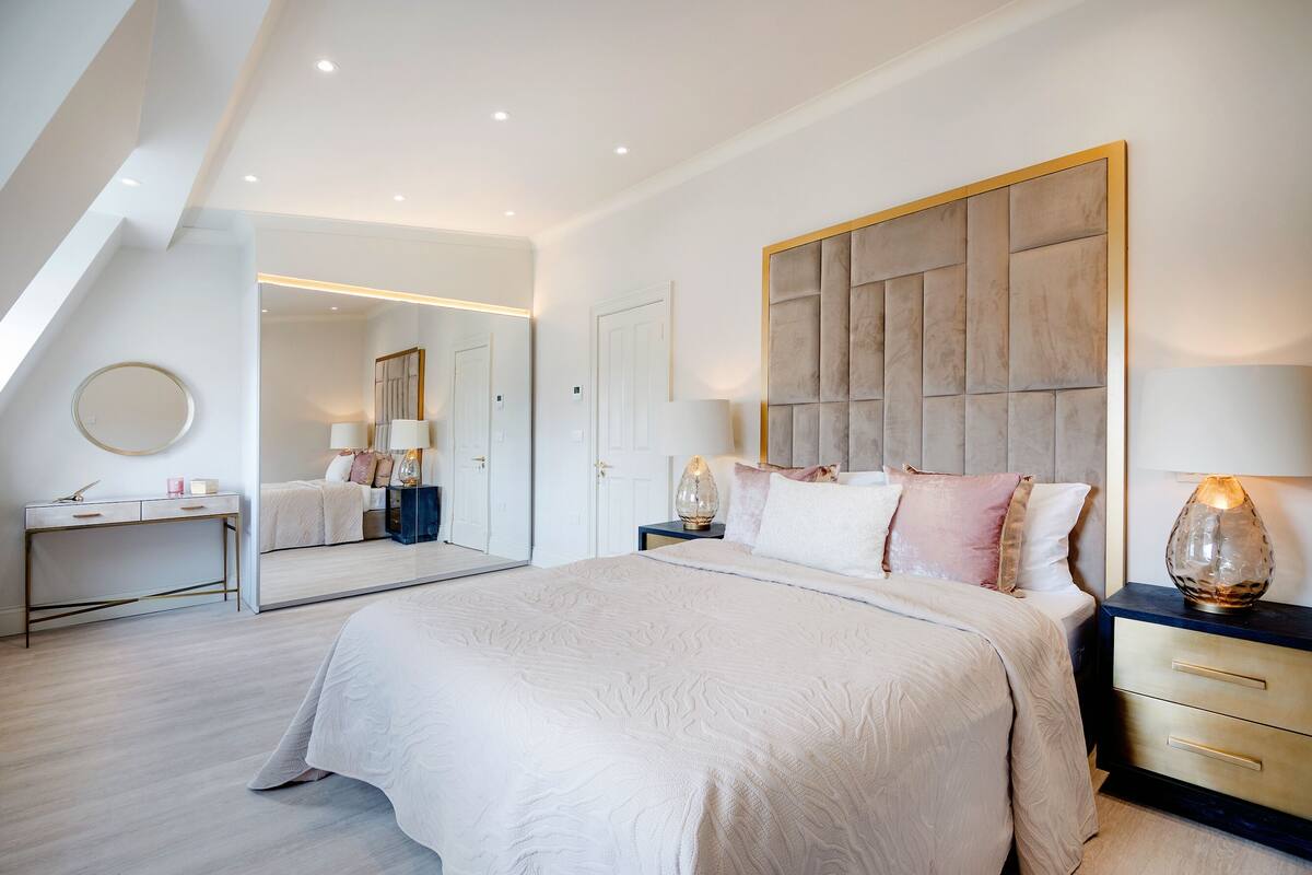 A modern bedroom with a large bed, bedside tables, a mirror, and a wardrobe.