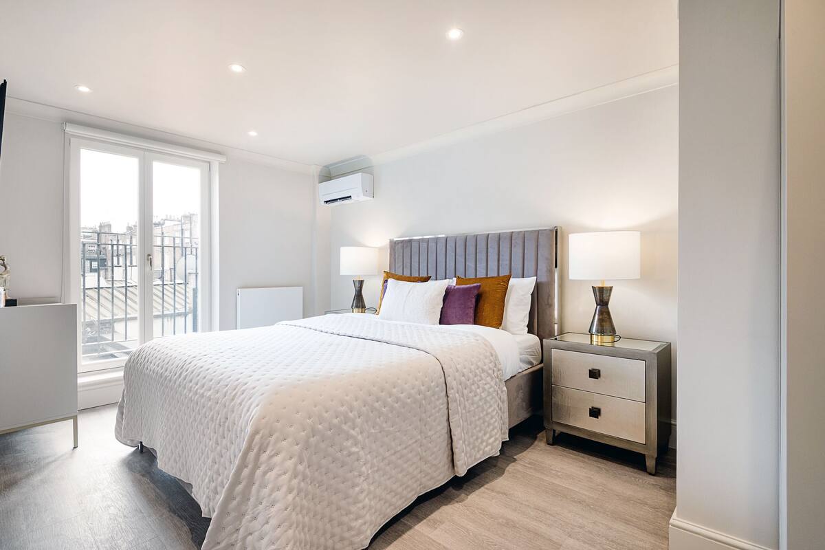 A modern bedroom with a large bed, bedside tables, and a window with a city view.