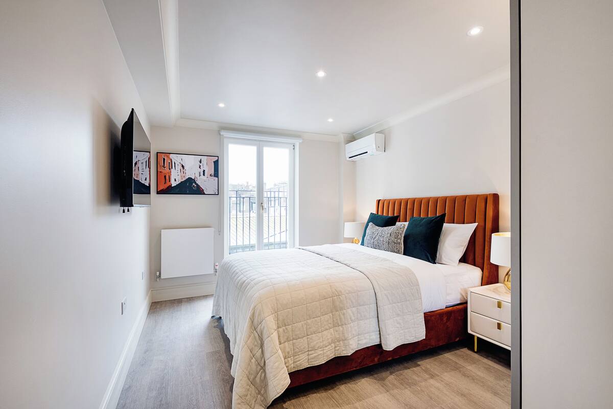 A modern bedroom with a large bed, a nightstand, and a wall-mounted TV.