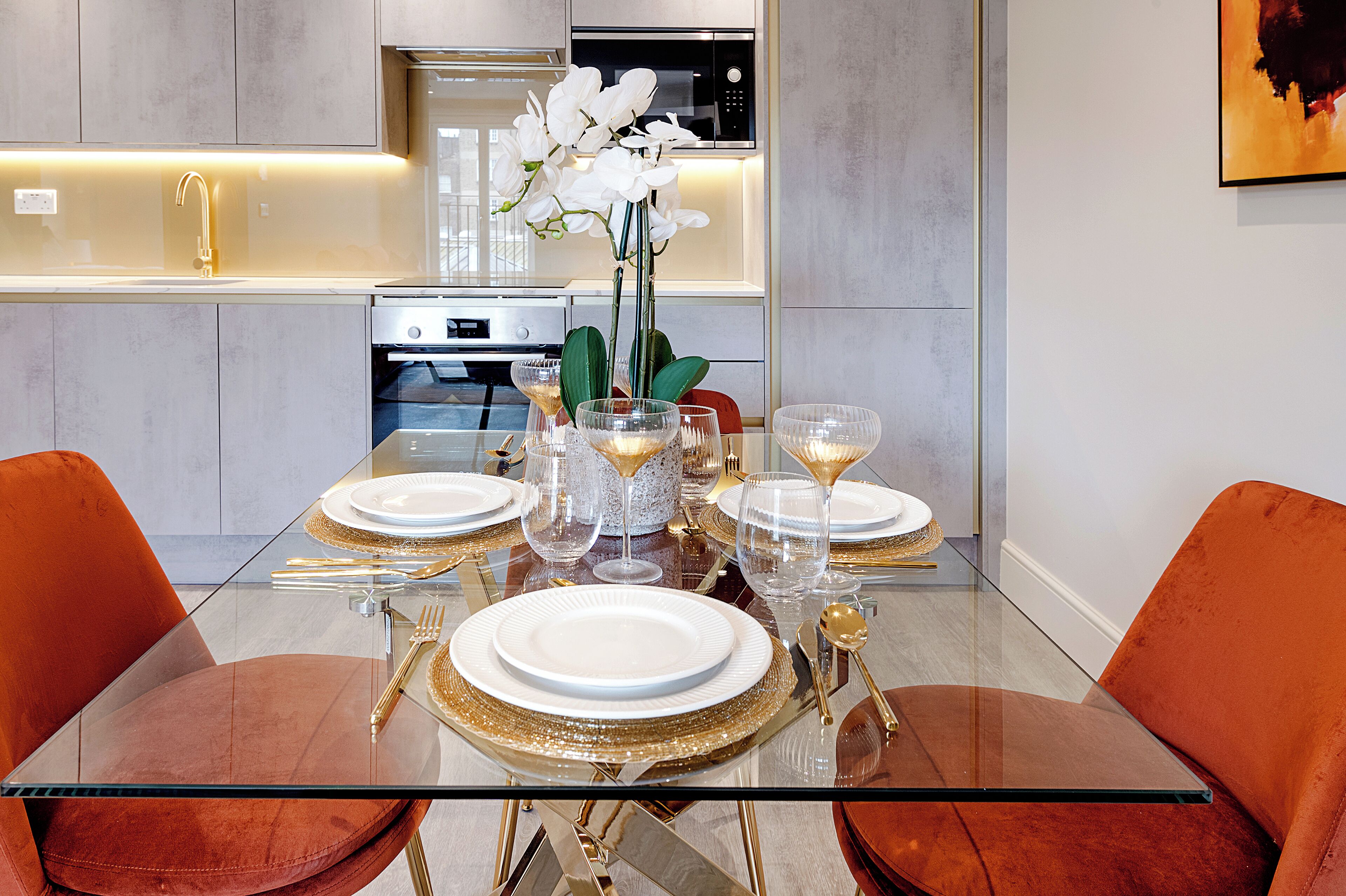Un comedor moderno con una mesa de vidrio dispuesta para cuatro personas, rodeado de sillas color naranja.