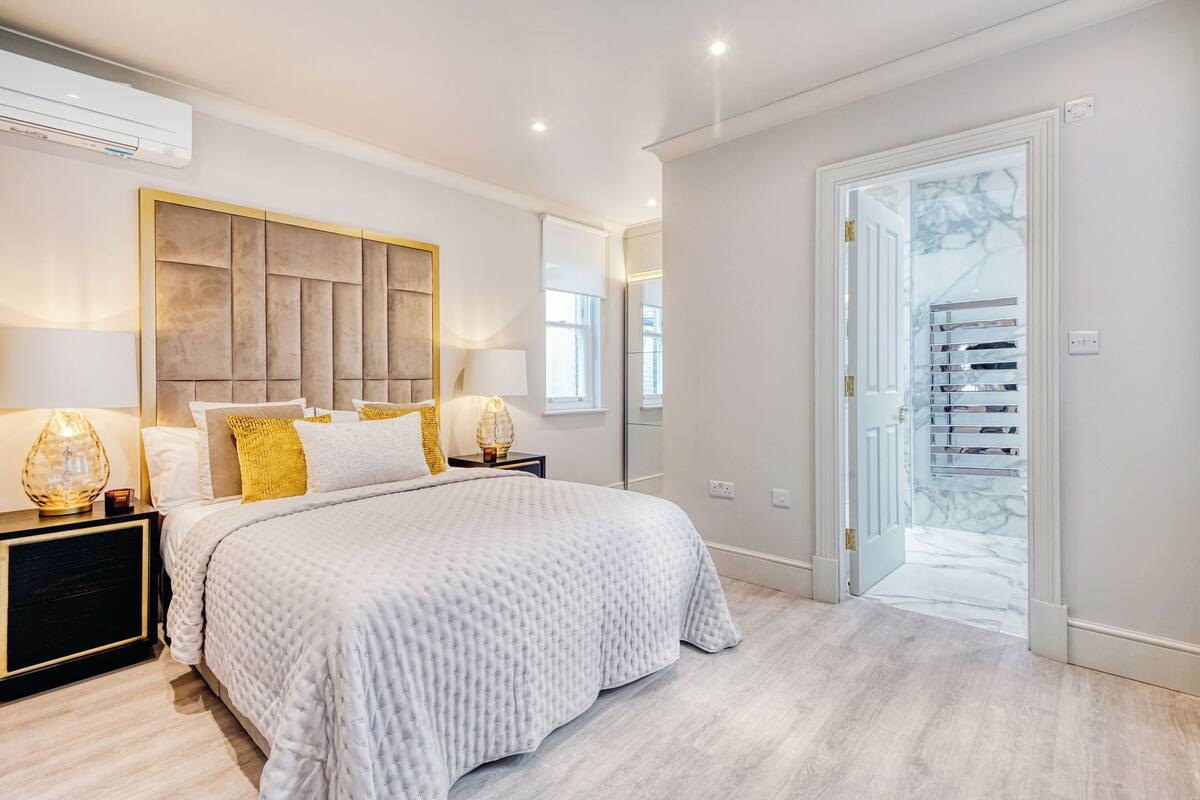 A modern bedroom with a large bed, bedside lamps, and a view of a staircase.