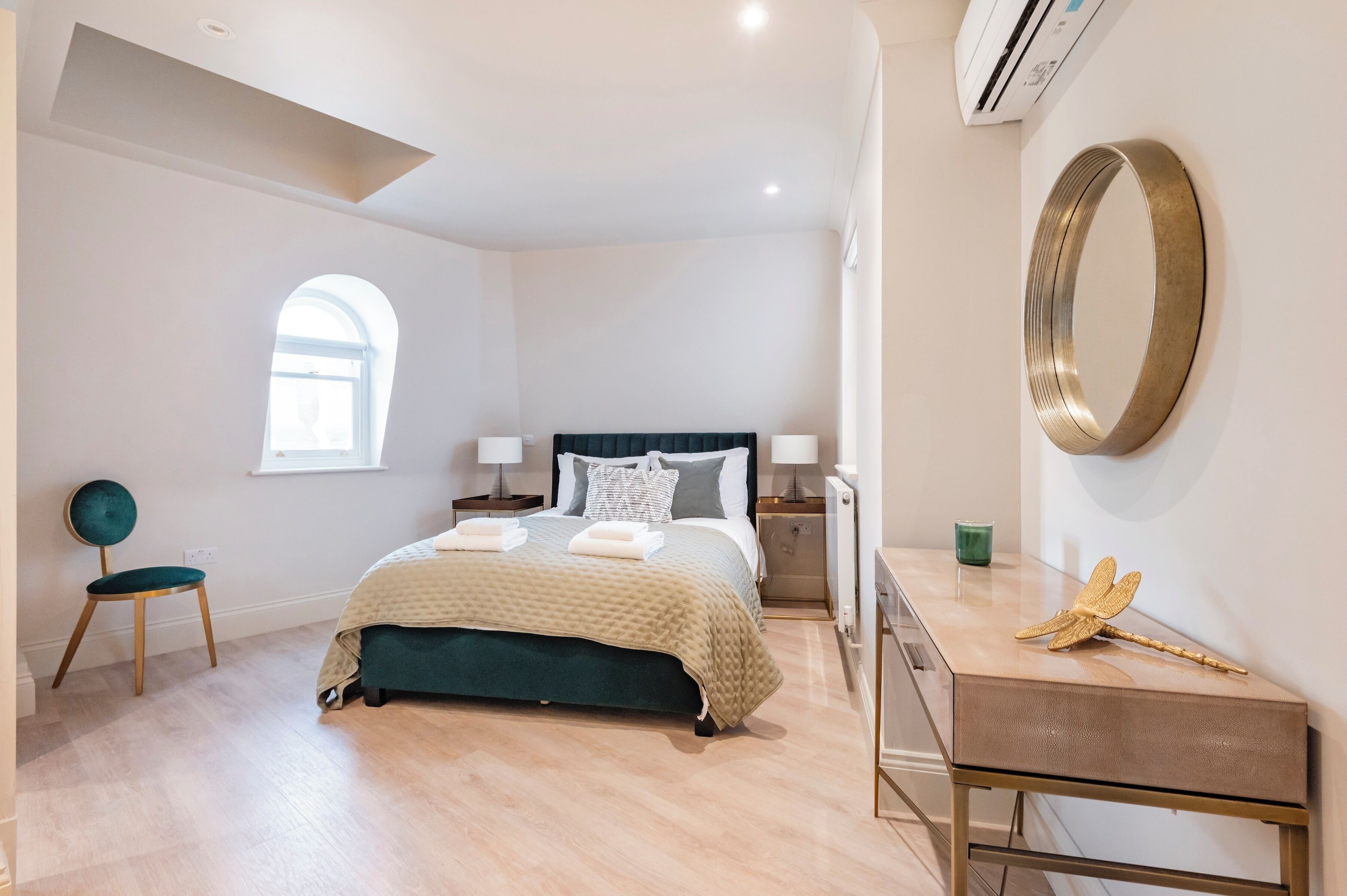 Un dormitorio moderno con cama, mesitas de noche, una silla, un escritorio y un espejo decorativo.