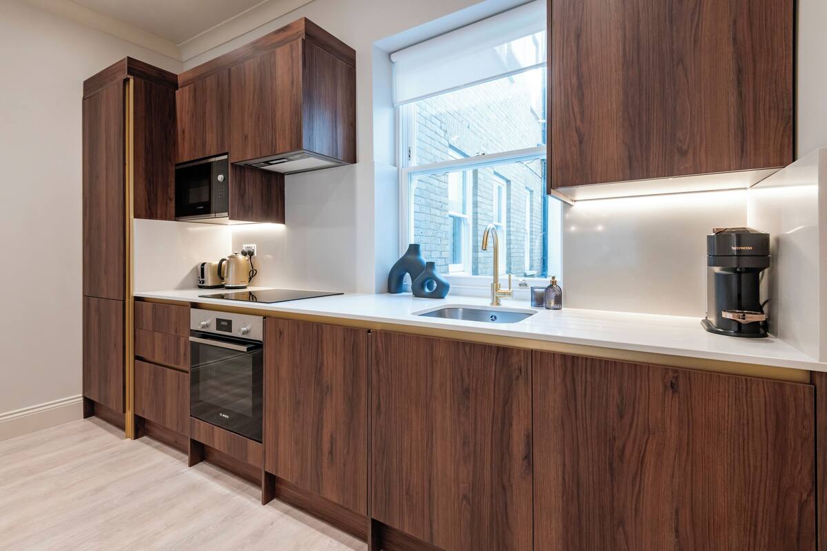 A modern kitchen with wooden cabinets, a built-in oven, a microwave, and a coffee machine.