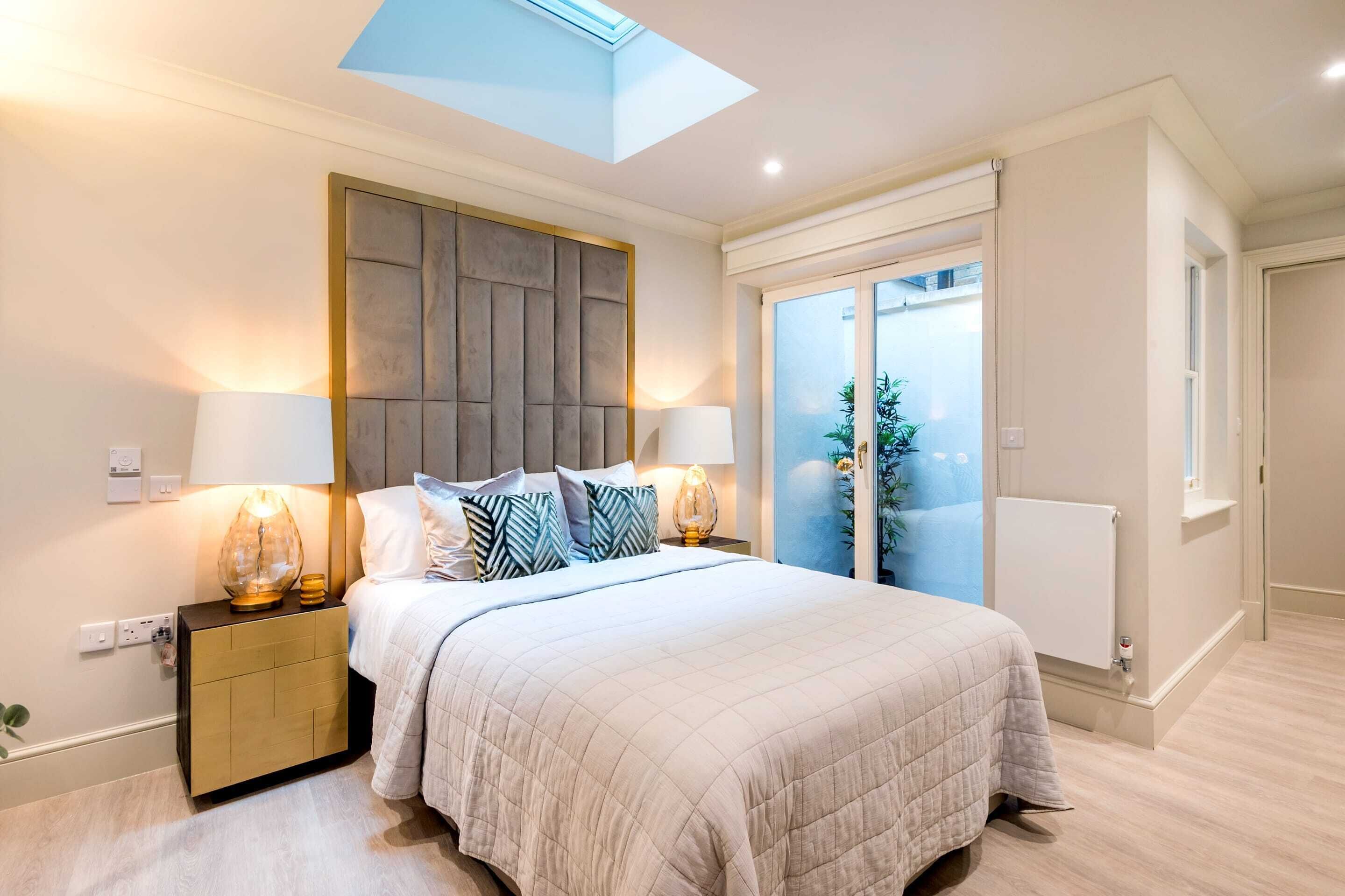A bedroom with a large bed, two bedside lamps, a wooden headboard, and a skylight.