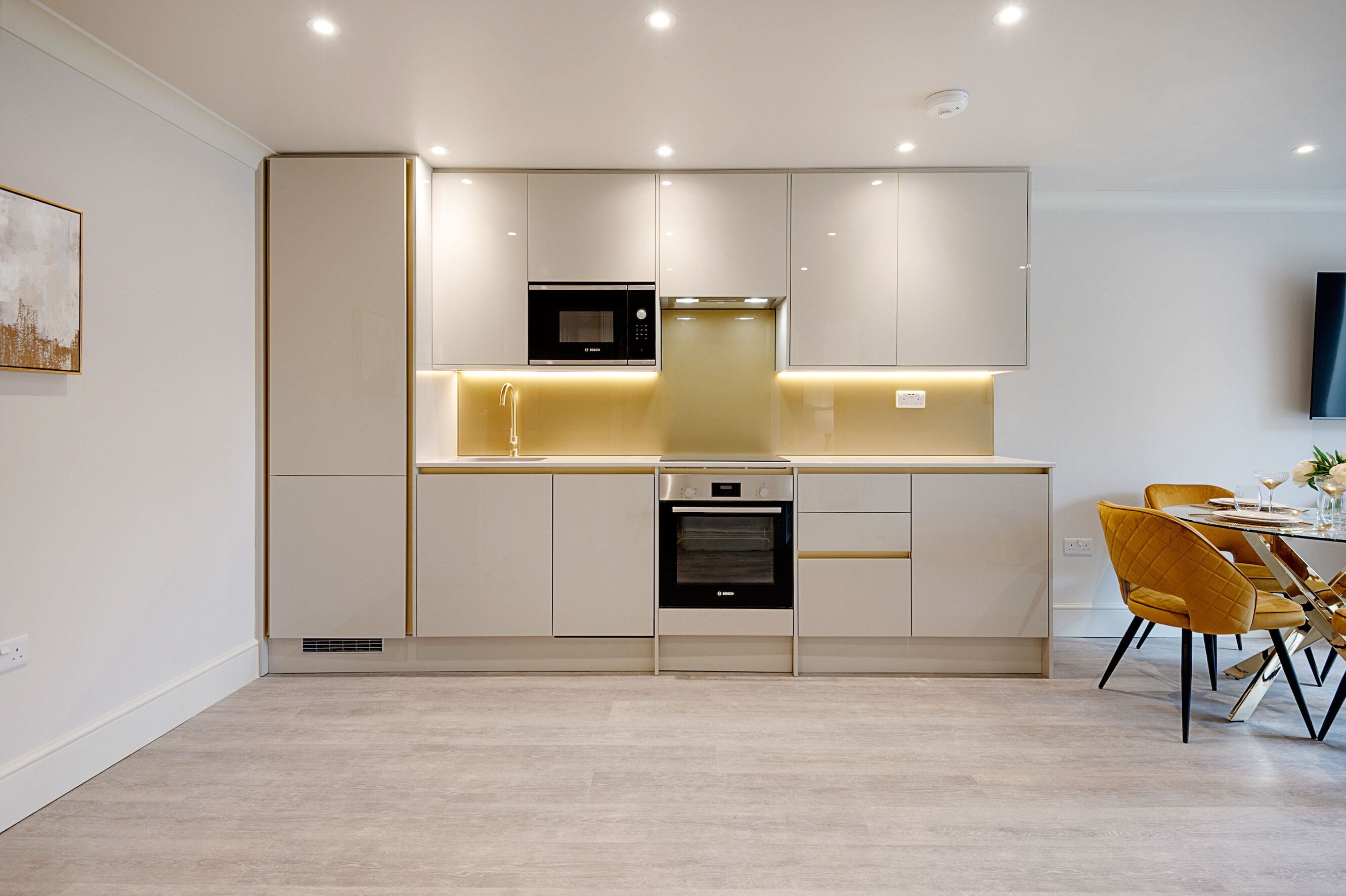Una cocina moderna con electrodomésticos integrados, un comedor con sillas amarillas y un televisor de pantalla plana montado en la pared.