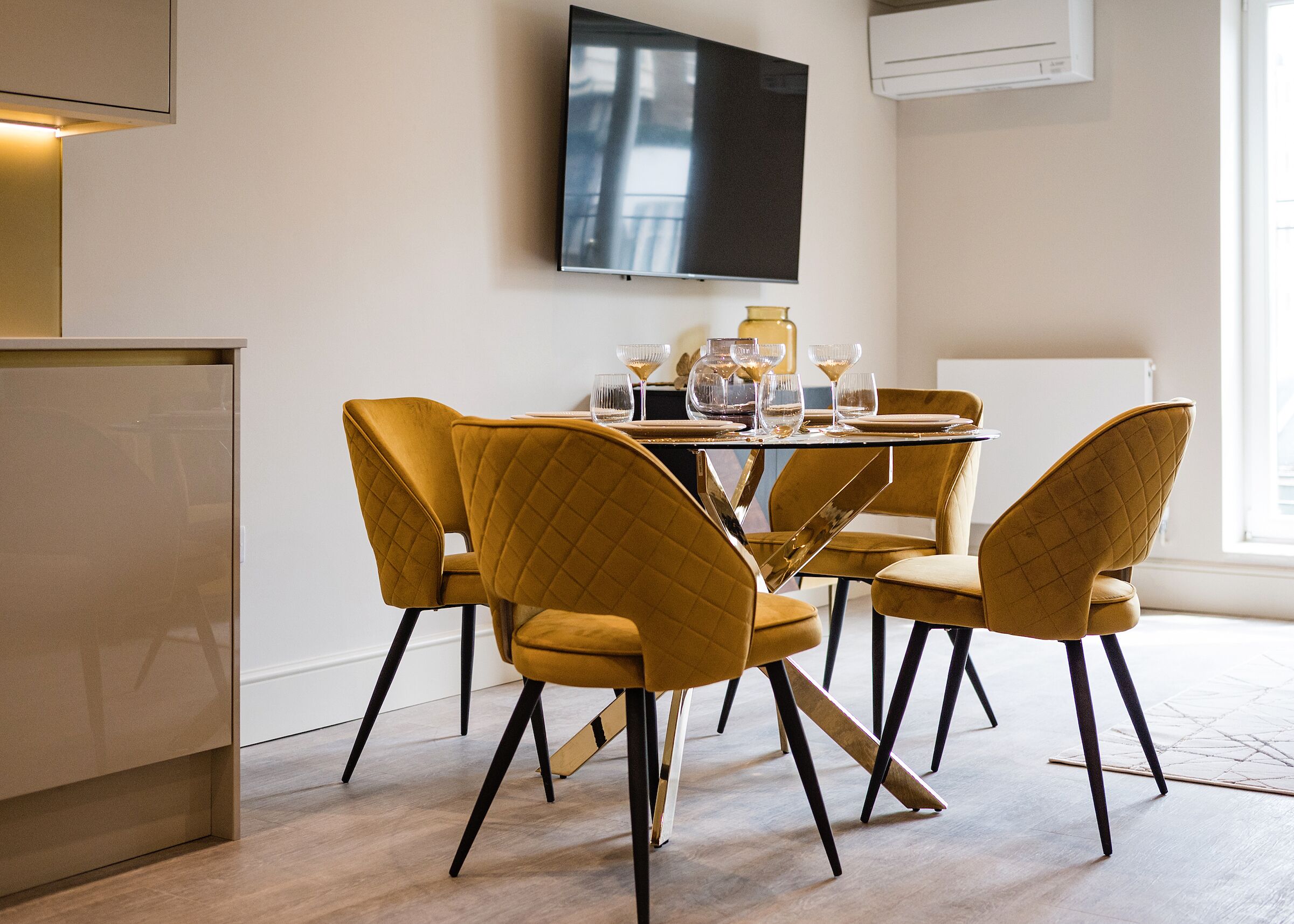 Un comedor con una mesa redonda, cuatro sillas y un televisor de pantalla plana montado en la pared.