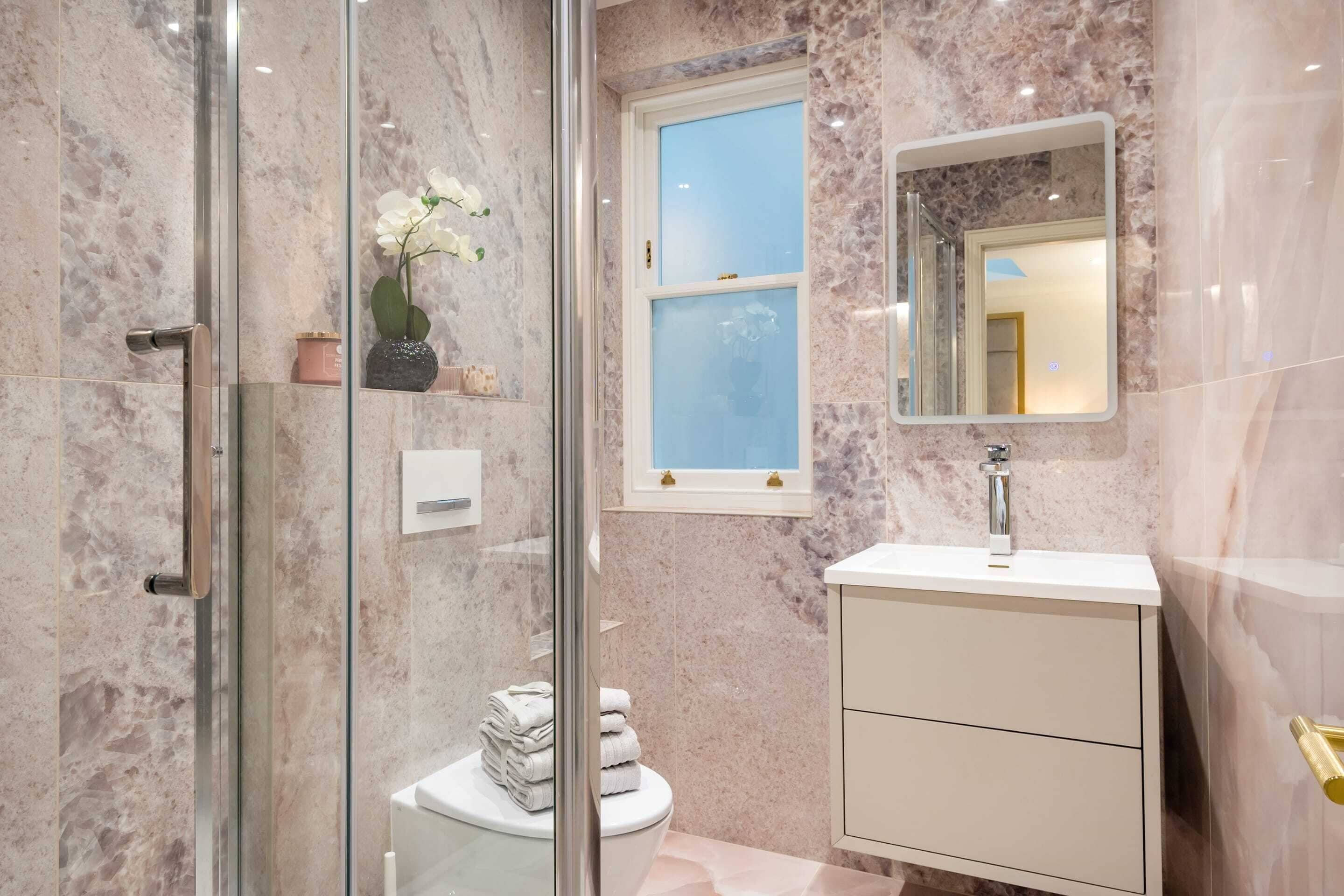 Une salle de bain avec une douche à parois de verre, des toilettes, un lavabo avec un miroir et des murs en marbre.