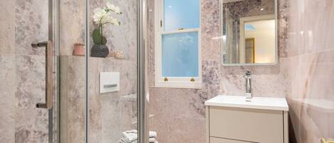 Une salle de bain avec une douche à parois de verre, des toilettes, un lavabo avec un miroir et des murs en marbre.
