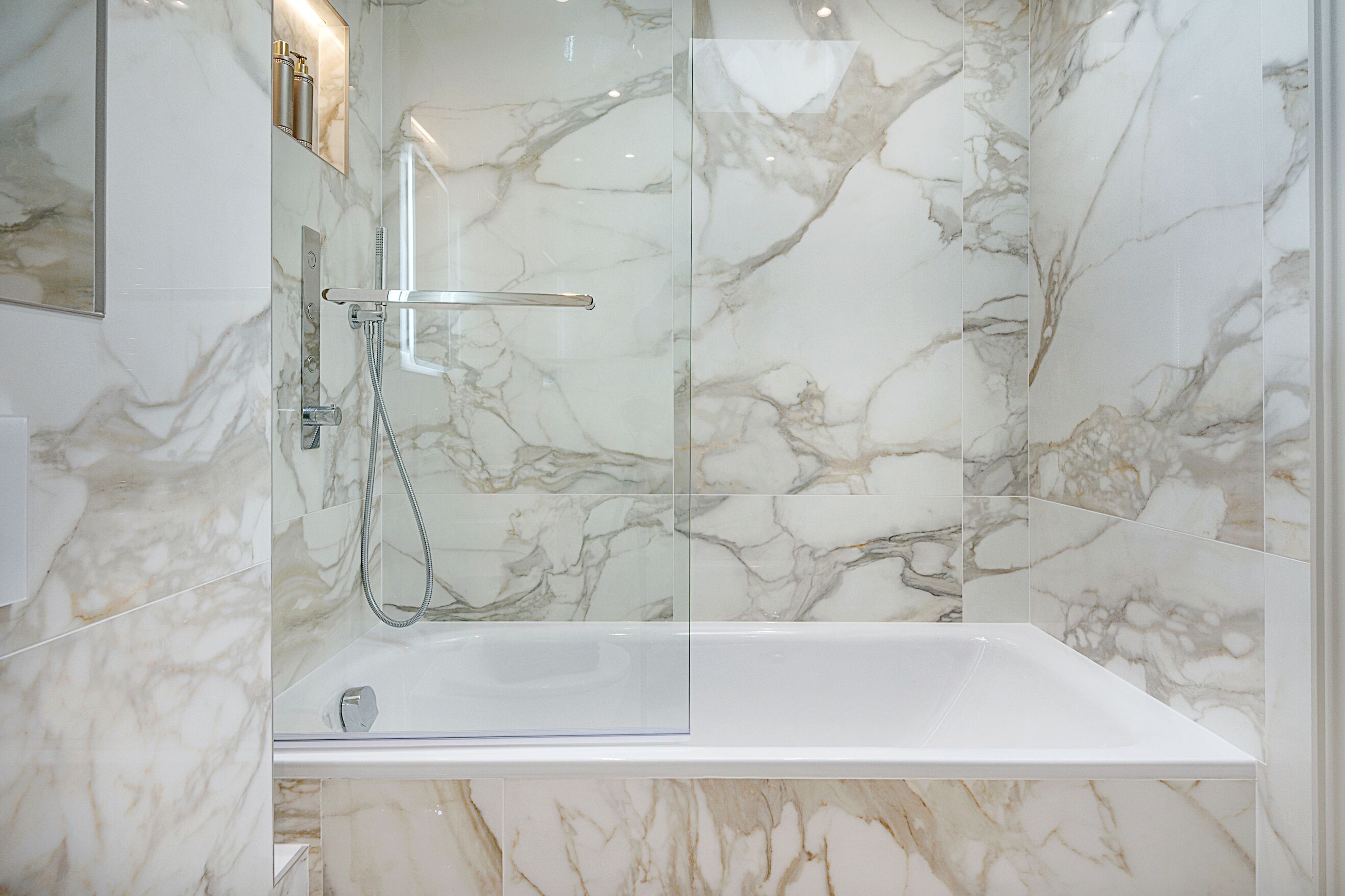 Een moderne badkamer met een glazen douchecabine en een wastafel van wit marmer.