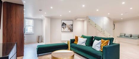 A modern living room with a green sofa, a round gold coffee table, and a staircase leading to an upper level.