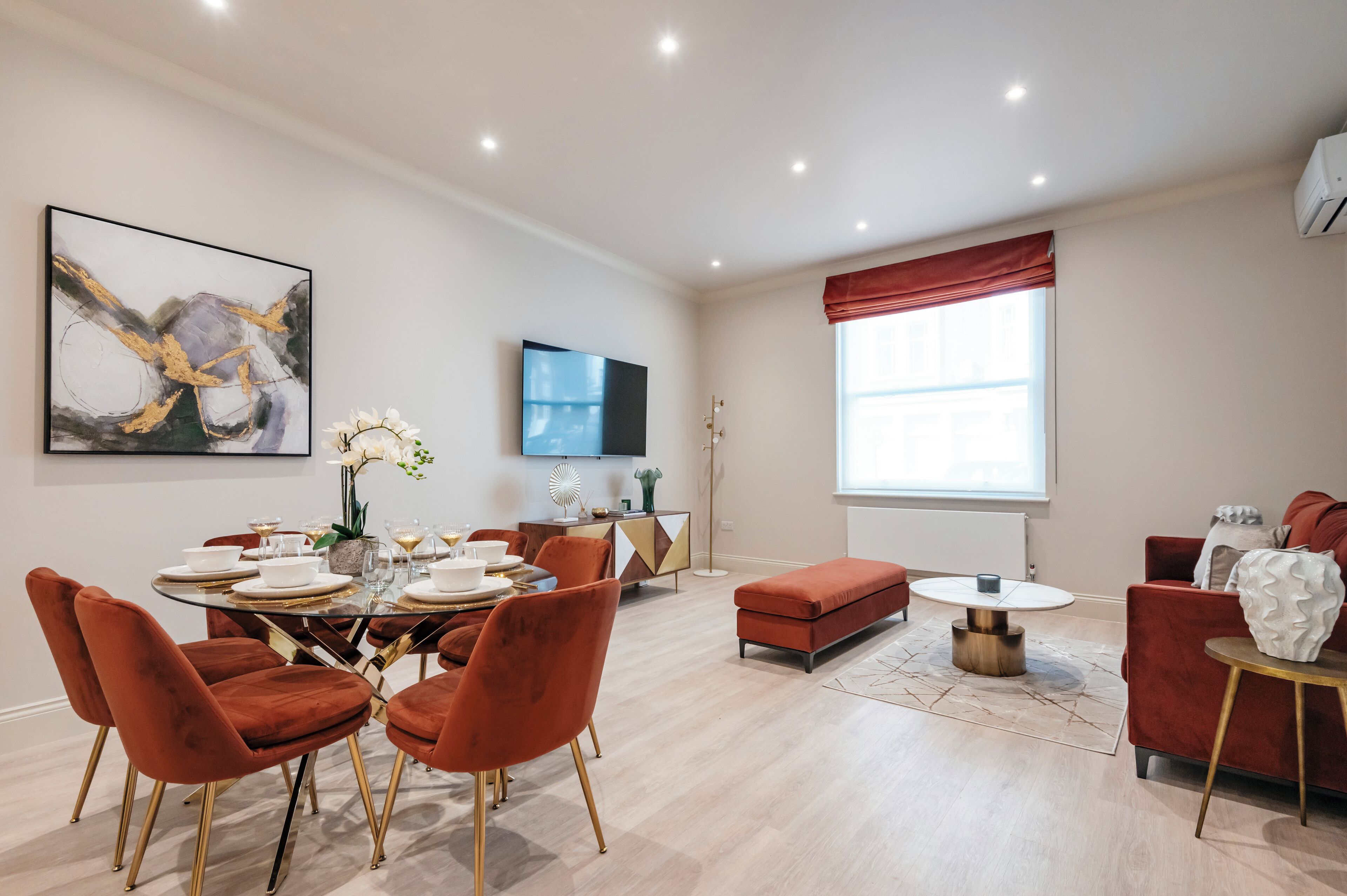 A modern living room with a dining area, red upholstered furniture, a flat-screen TV, and a large abstract painting.