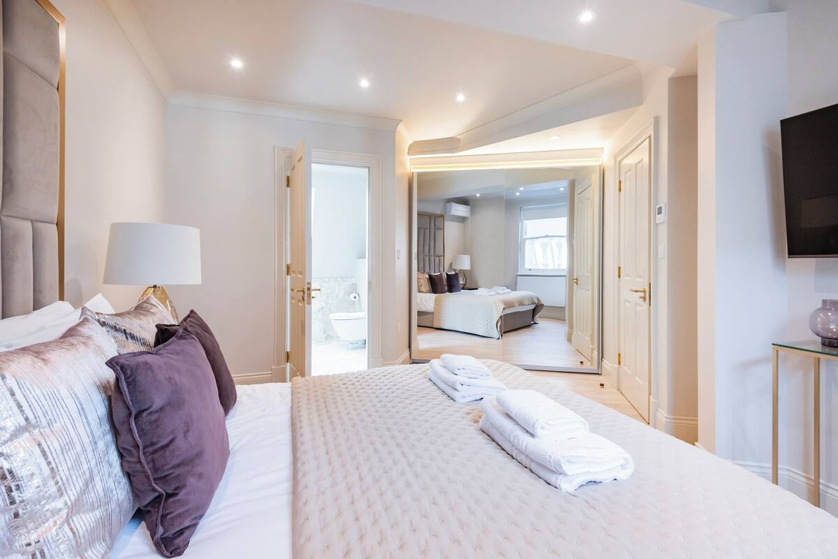 A modern hotel room with a large bed, a sitting area, and a bathroom visible through an open door.