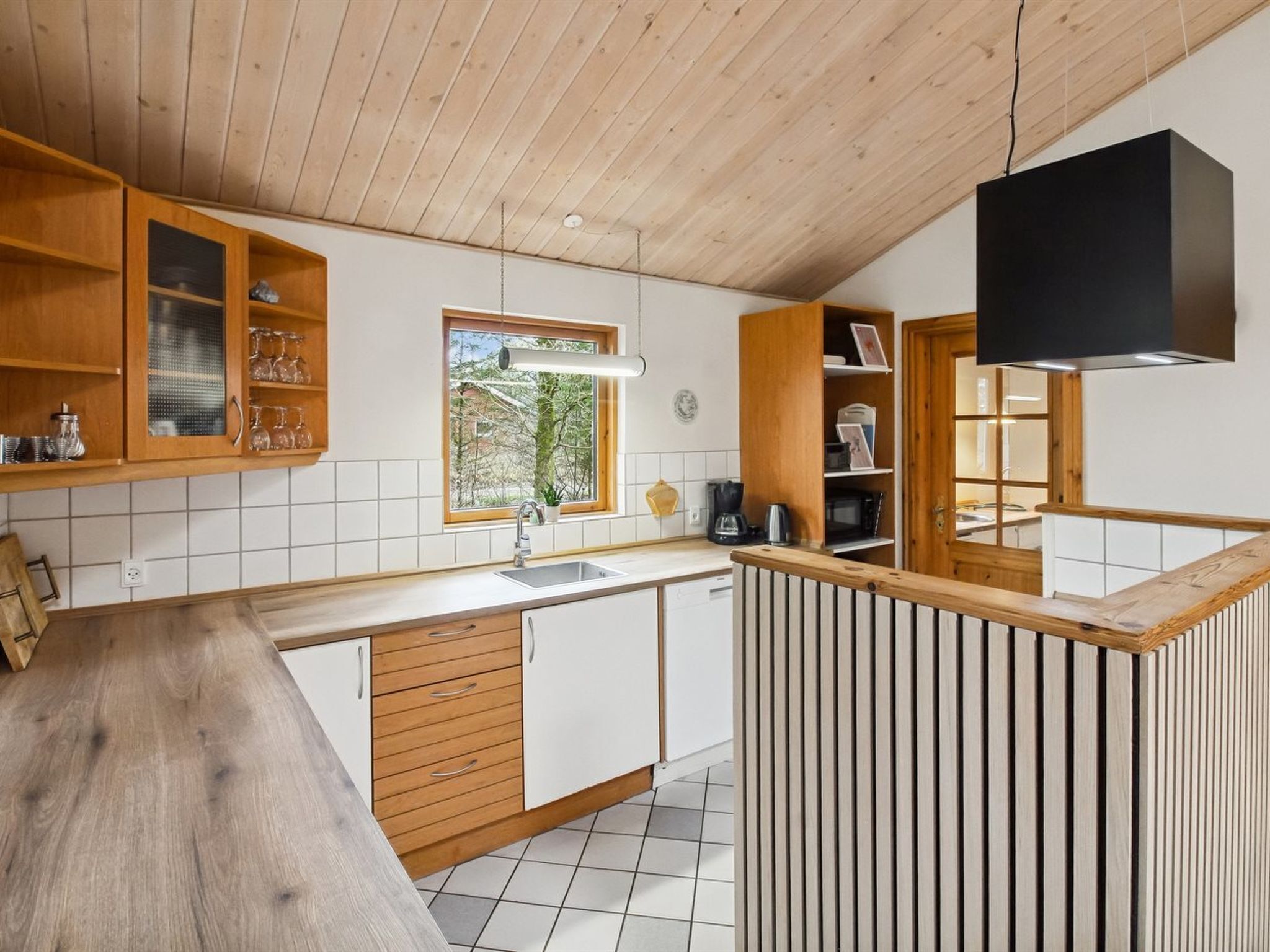 Una cocina moderna con armarios de madera, un ventanal grande y una lámpara colgante negra.