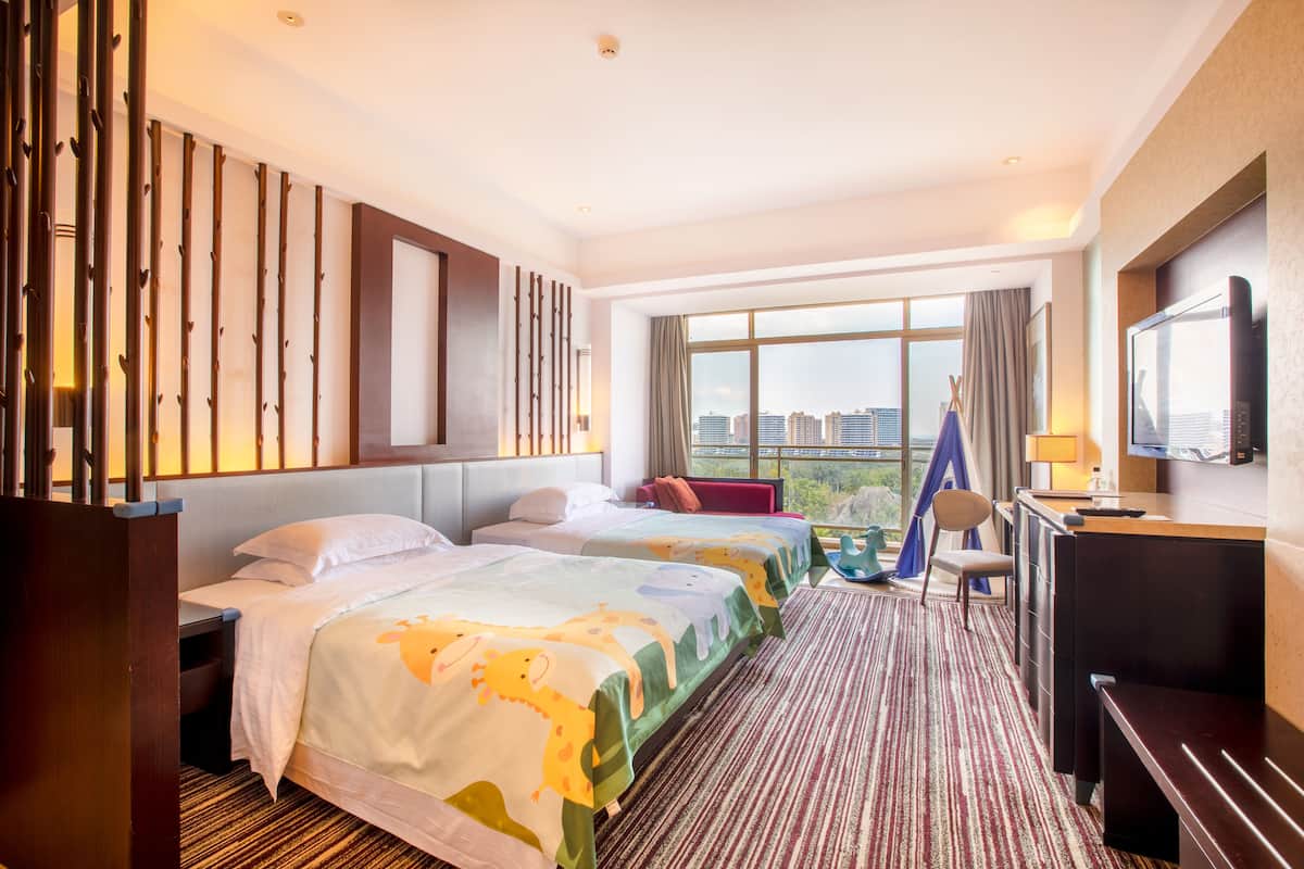 A hotel room with two beds, a desk, a TV, and a city view.