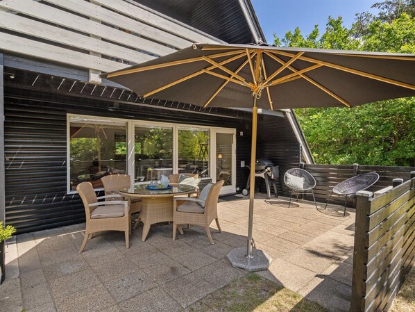 Une terrasse extérieure avec une table et des chaises, un barbecue et un grand parasol.