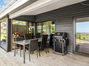 Une terrasse extérieure avec une table et des chaises, un barbecue et une porte-fenêtre coulissante donnant sur une véranda.