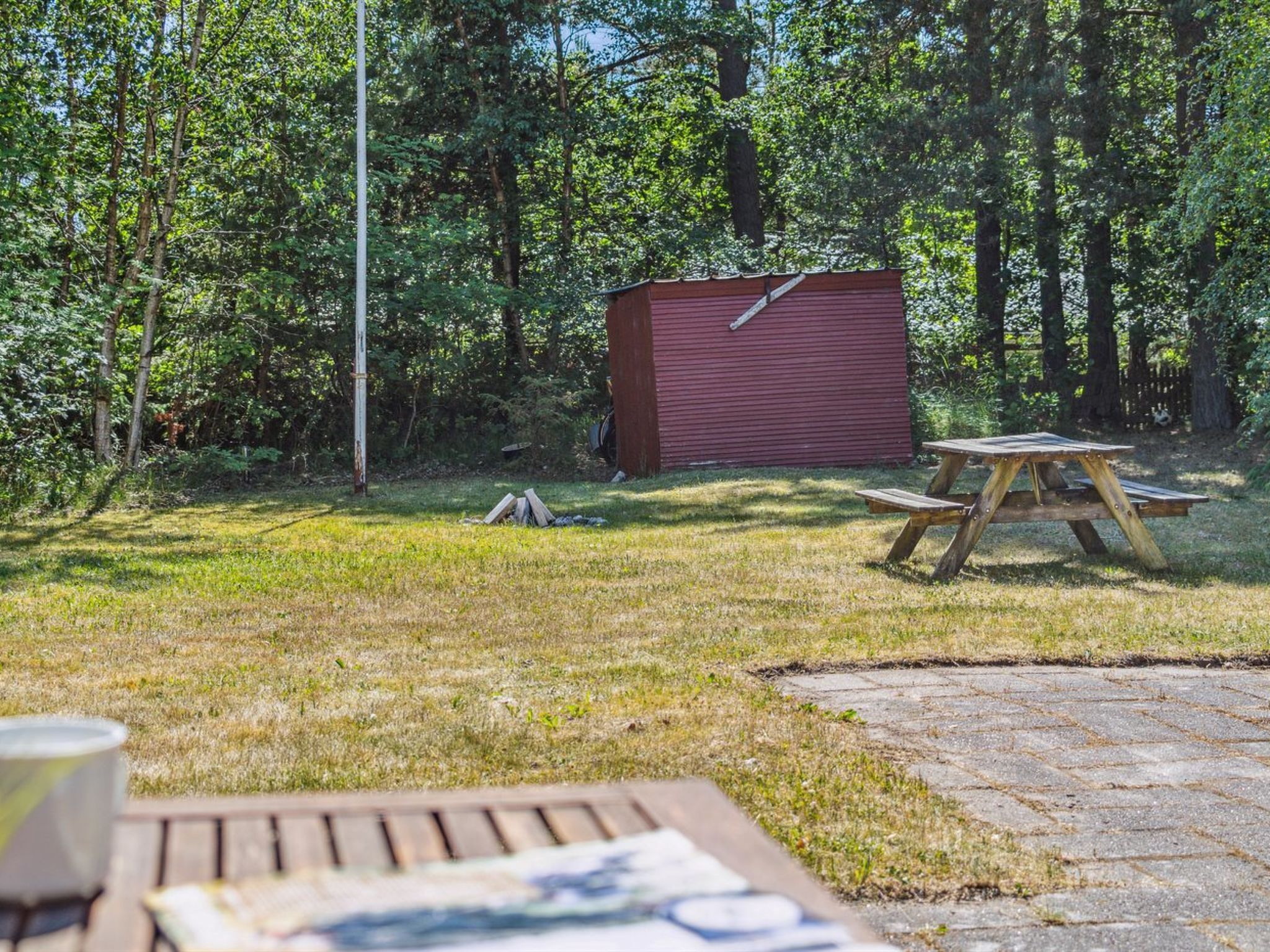 En röd förrådsbyggnad i ett skogsområde, med ett picknickbord och en asfalterad gångstig.
