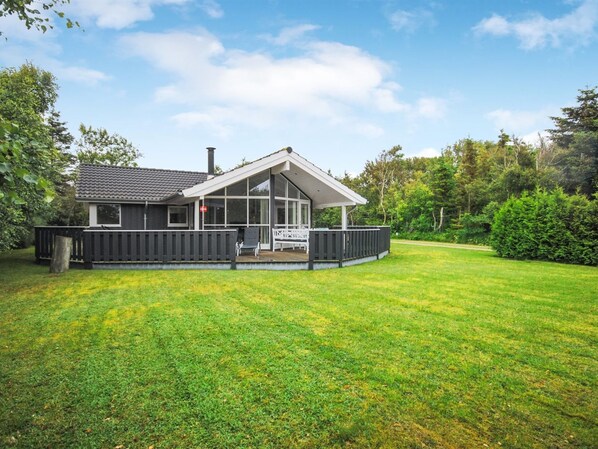 Ein modernes Haus mit großer Veranda, umzäuntem Garten und gepflegtem Rasen.