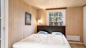 A bedroom with a wooden ceiling, a large window, a bed with white bedding, a wall-mounted light, and a radiator. - "Daliborka" - 600m from the sea by Interhome (Hals)