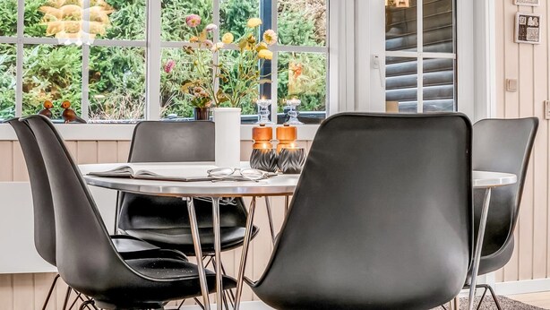 A modern dining area with a round table and black chairs, large windows with a view of greenery, and a pendant light fixture. - "Daliborka" - 600m from the sea by Interhome (Hals)