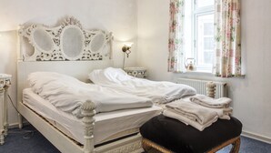 A neatly made bed with white linens, a decorative headboard, a bedside table with a lamp, and a window with floral curtains. - "Ahvo" - 22km from the sea by Interhome (Bredebro)