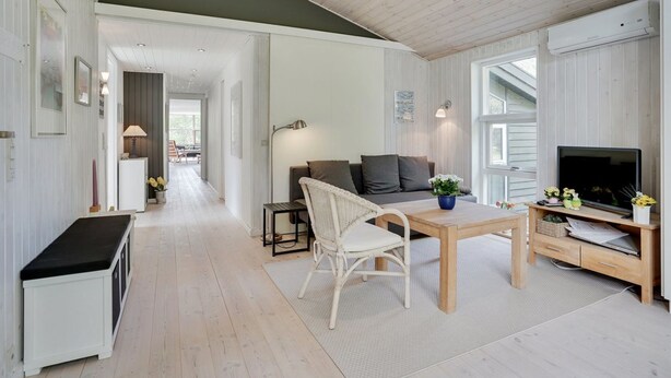Un espacio habitable moderno y de planta abierta, con zona de comedor, sofá, televisión y pequeña cocina.